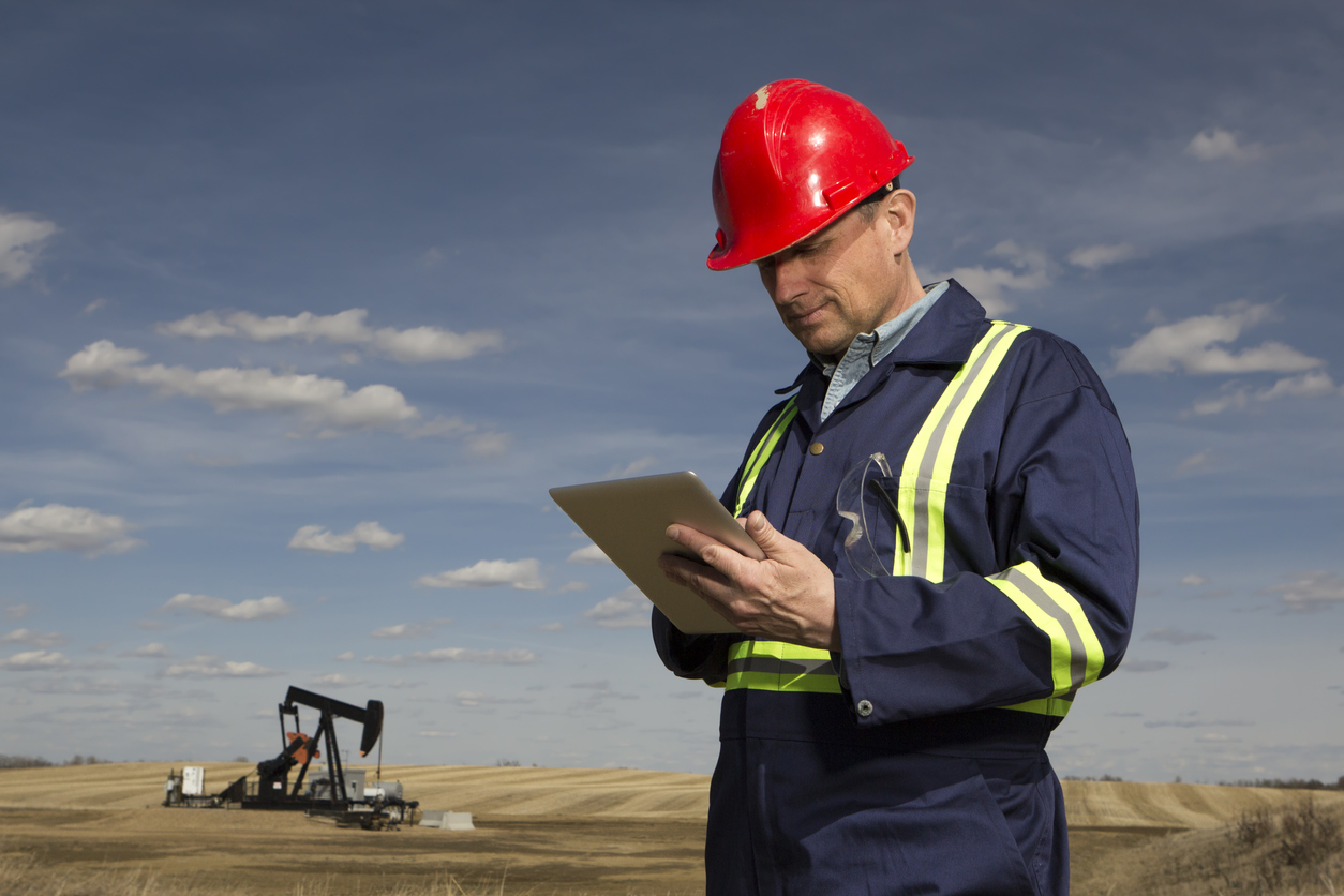 oil field employee on tablet with oil derrick in background